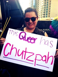 Writer with a sign that reads: "This Queer has Chutzpah"